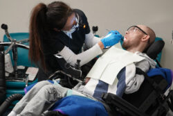 ACRC individual Charles sits in a wheelchair in a dentist office and smiles at the medical staff treating him.